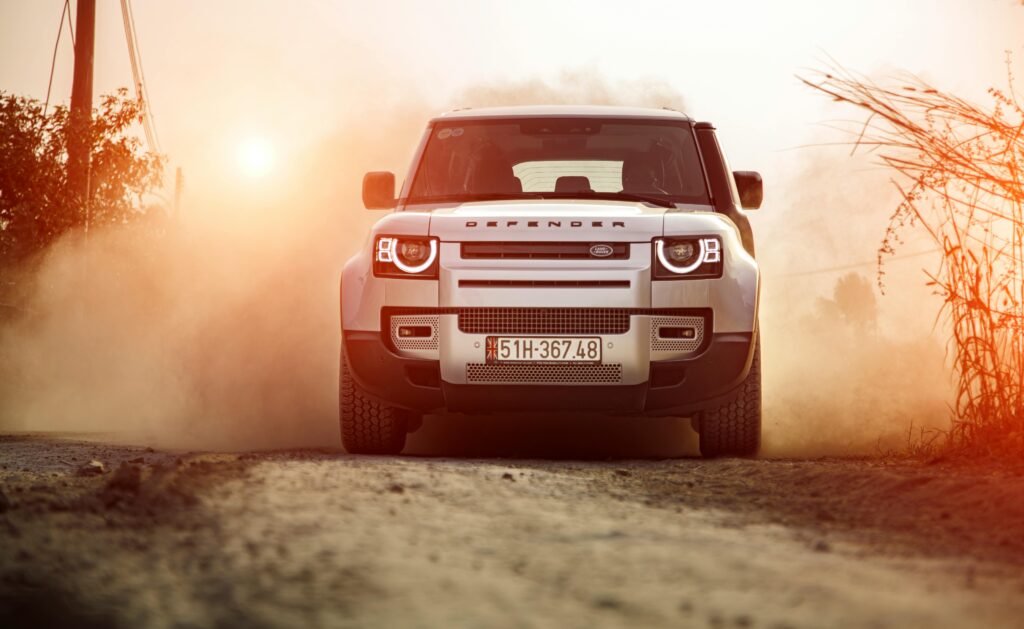 pexels-photo-14901782-14901782 Land Rover Defender driving on a dusty road at sunset, embodying adventure and rugged capability.